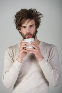 Dağınık saçlı adam mulled şarap iç. Sabah kahve veya süt ile. Uykusuzluk, ferahlık ve enerji. Çay bardağı gri arka plan üzerinde uykulu adamla. Soğuk algınlığı ve grip, tek.
