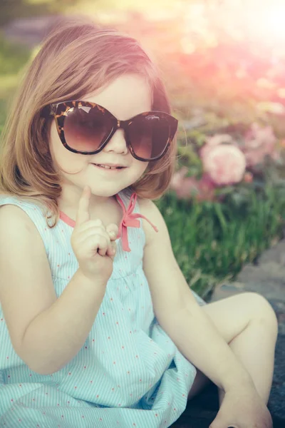 Criança em óculos de sol sentado no parque em ambiente floral — Fotografia de Stock