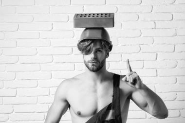 genç yakışıklı maço adam Oluşturucu ile seksi atletik güçlü vücut mavi üniformalı güçlü elleri ve turuncu baret veya kask tuğla beyaz tuğla duvar arka planda tutan kas sakallı