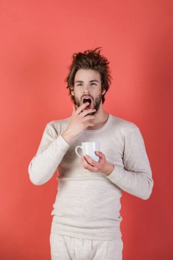Morning with coffee or milk. Sleepy guy with tea cup on red background. Man with disheveled hair drink mulled wine. Cold and flu, single. Insomnia, refreshment and energy. clipart