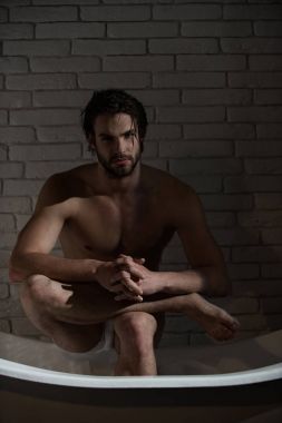 Banyo ve ev konfor. Spa ve rahatlama, seksi bir adam. Küvet içinde oturan ıslak saçlı çocuk. Banyo kas vücut olan adam. Hijyen ve sağlık.