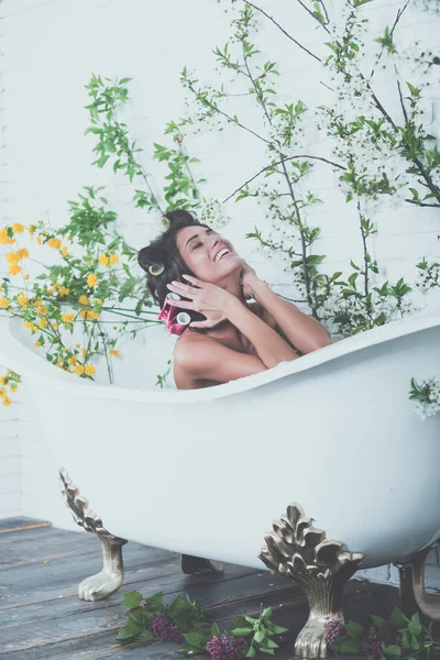 Woman with curlers on hair sit in bath, body care. — Stock Photo, Image