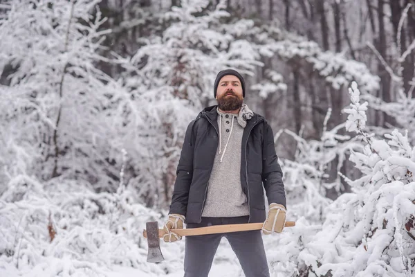 Bebaarde man met bijl in het besneeuwde forest. — Stockfoto