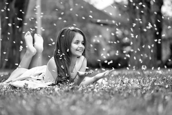 Dziewczynka na zielonej trawie z płatkami — Zdjęcie stockowe