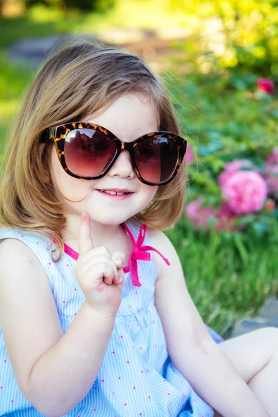 Дівчина посміхається з піднятим пальцем в літньому саду — стокове фото