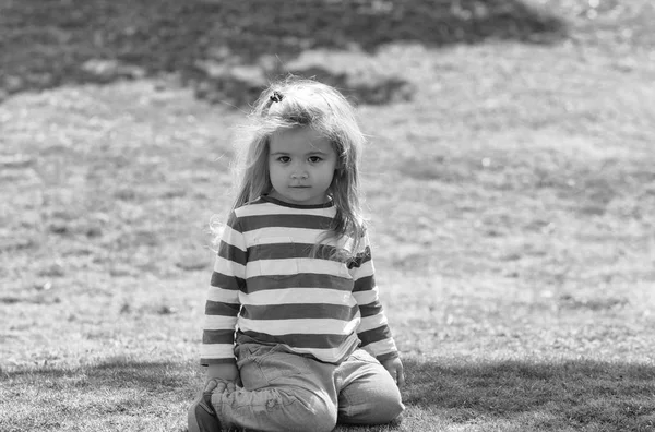 Netter kleiner Junge sitzt auf grünem Gras im Park — Stockfoto