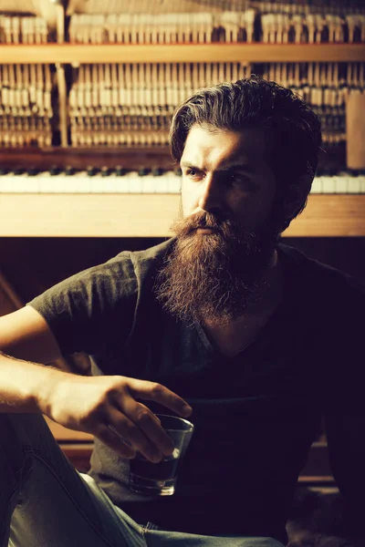 Бородатый мужчина со стеклом рядом с деревянным фортепиано — стоковое фото