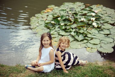 Çimlenme ve büyüme. Kızlar çim gölet nilüfer çiçekleri ile oturmak. Gelecek ve gelişen. Çocuk mutlu Yeşil Göl Manzara üzerinde gülümse. Yaz tatil kavramı.