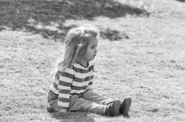 Söt glad pojke som sitter på gräset i parken — Stockfoto