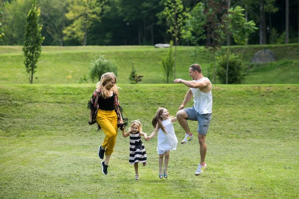 Children and parents jump on green grass. Girls, woman and man smile on summer landscape. Mothers and fathers day. Happy childhood, family, love. Freedom, activity, lifestyle, energy concept.