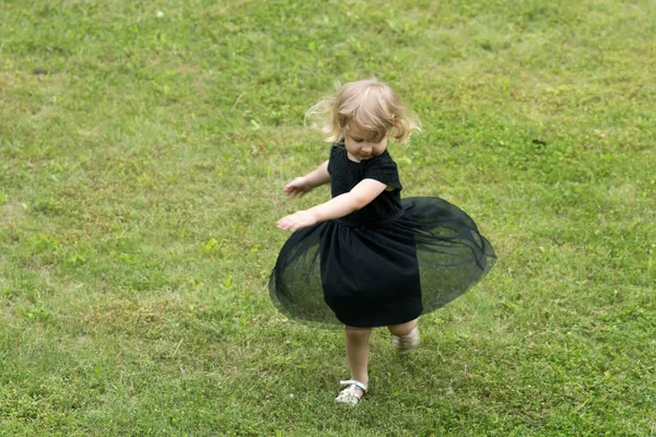 緑の草に黒のドレスでブロンドの髪のスピンを持つ少女 夏休み 楽しみ 概念冒険 — ストック写真