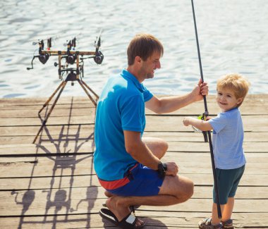 Aile, babalar günü, çocukluk. Balıkçılık, olta balıkçılığı, etkinlik, macera. Tatil, hobi, yaşam tarzı. Ahşap iskele üzerinde çubuklar ile balık tutan adam ve çocuk çocuk. Babası küçük oğlu içinde tatlı su balık tutmayı öğretmek.