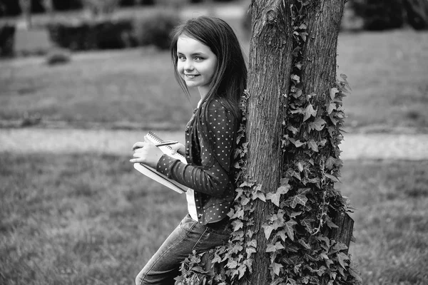 Ragazza con taccuino e penna vicino albero — Foto Stock