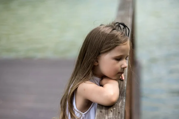 Meisje kind met lange haren kijken naar water vanuit bridge — Stockfoto