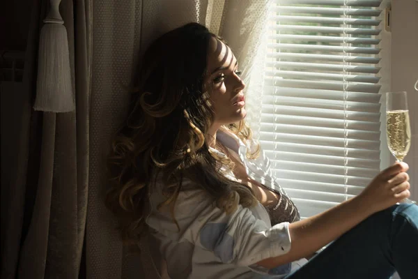 Жінка з довгим кучерявим волоссям п'є шампанське у вікні — стокове фото