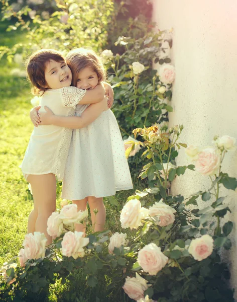 As crianças que sorriem em flores de rosa florescentes — Fotografia de Stock