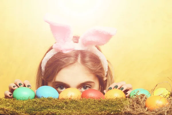 Feliz Pascua chica oculta en orejas de conejo con huevos de colores — Foto de Stock