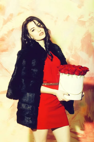 Söt flicka iklädd röd klänning poserar med rosor i låda — Stockfoto