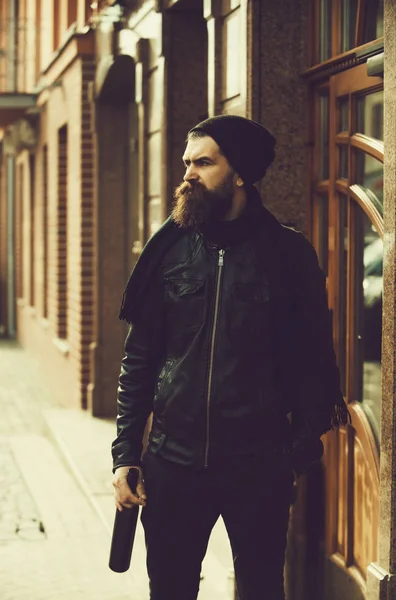 Homme barbu sérieux hipster avec bouteille de vin en veste en cuir — Photo