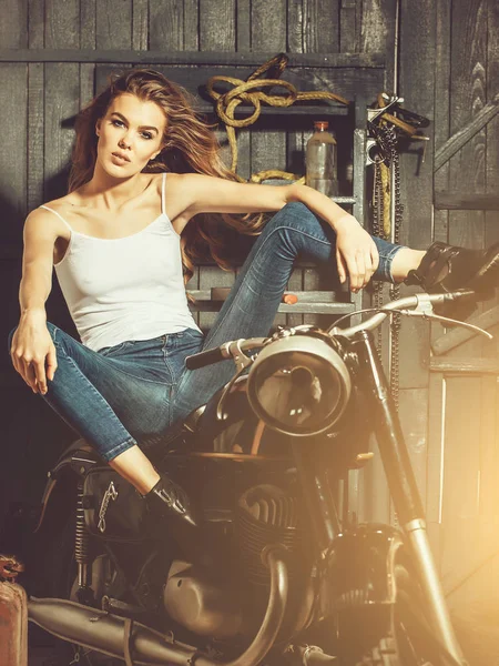 Menina motociclista sentado na motocicleta vintage na garagem — Fotografia de Stock