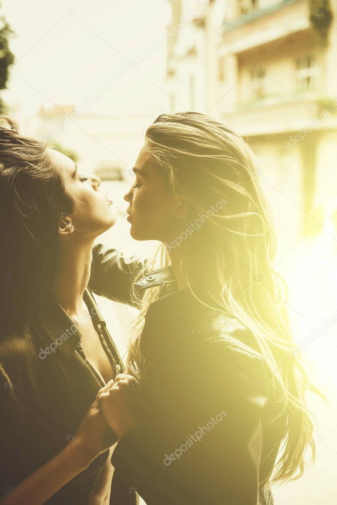 Two sexy women or sexi girls with beautiful, long hair hugging on sunny day outdoors on urban background. Lesbian couple. Love and desire