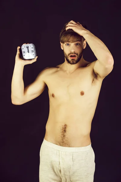 Morning, handsome muscular man with alarm clock on black backgro — Stock Photo, Image