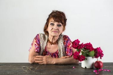 Yaşlı kadın poz çiçekler, elma, tablo üzerinde gözlük ile.
