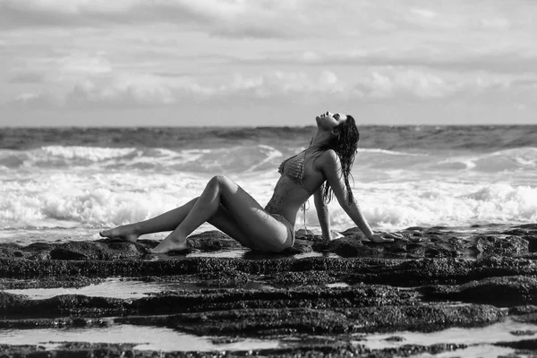 Красива дівчина в сексуальному жовтому купальнику, що сидить на кам'янистому пляжі — стокове фото
