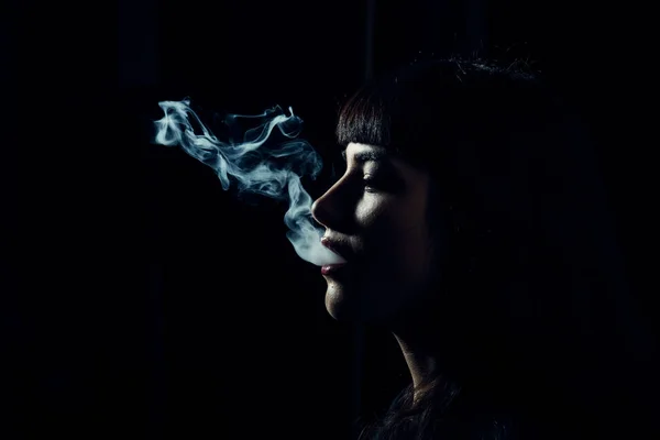 Femme tête avec de la fumée dans la bouche sur fond noir . — Photo