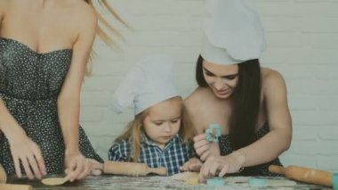 Mutlu aile birlikte fırın hazırlıyor. Anne ve kız çocuk kurabiye pişiriyor ve mutfakta eğleniyorlar. Ev yapımı yemek ve küçük bir yardımcı..