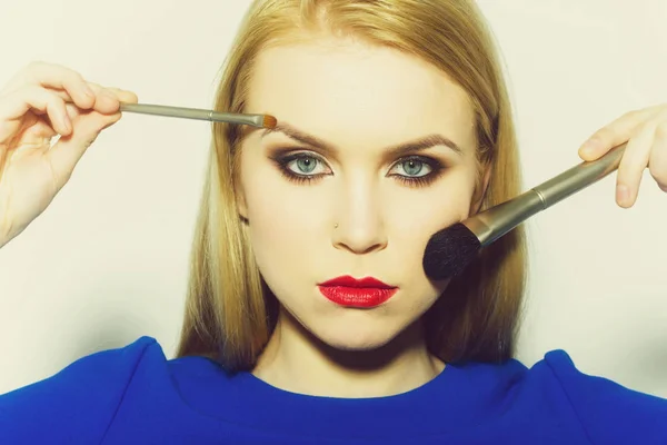 Woman with brushes applying powder and makeup on face