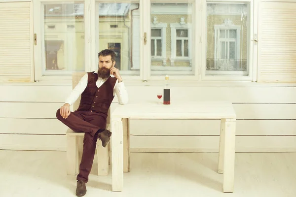 Hipster sentado na cadeira à mesa com garrafa e vidro — Fotografia de Stock