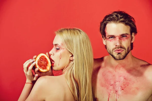 man and woman with makeup hold grapefruit