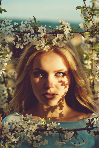 Spring and youth, Pretty girl or cute woman posing with adorable face, stylish makeup and blond, long hair in floral frame of white, blossoming flowers on sunny day on blurred natural environment.
