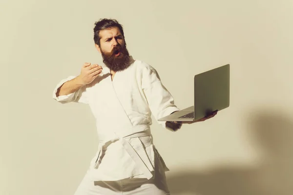 bearded serious karate man in kimono with laptop