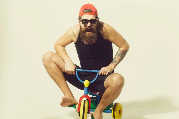 Bearded happy man on colorful bicycle toy in sunglasses, cap — Stock Photo, Image