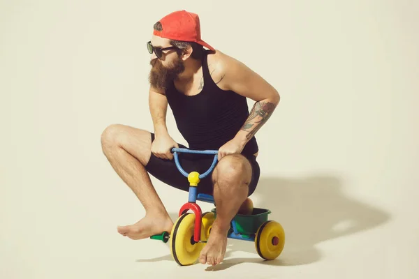 Бородатий чоловік на барвистій велосипедній іграшці в червоній шапці — стокове фото