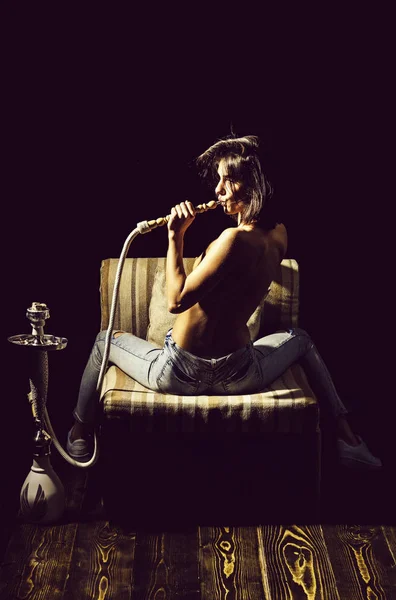Сексуальная девушка с голым телом, курящая кальян в джинсах — стоковое фото