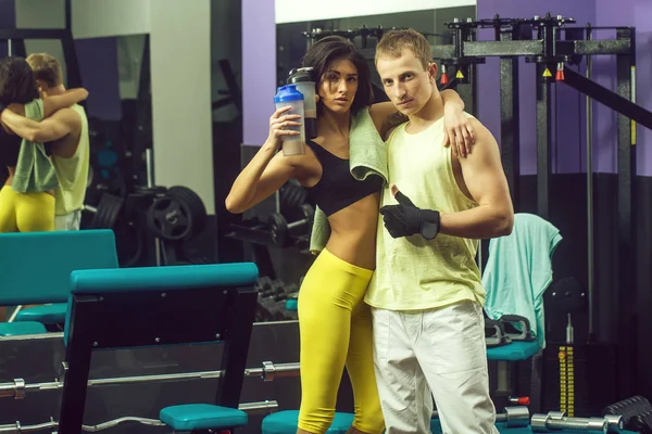 Muskulös man och sexig tjej på gym tränare med flaska — Stockfoto