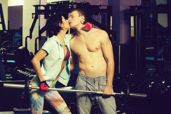 Muscoloso uomo e ragazza in palestra con baci con bilanciere — Foto Stock