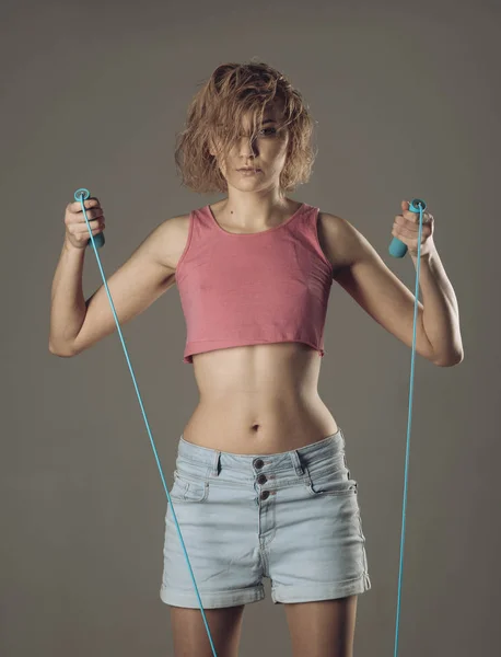 Girl with untidy hair does exercises with jump rope.