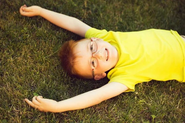 Happy babyjongen met rood haar in glazen op gras — Stockfoto