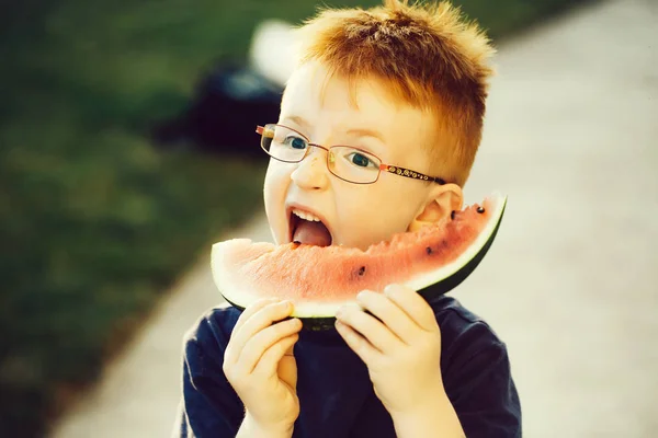 Gelukkige jongen met rood haar in glazen eten van watermeloen — Stockfoto