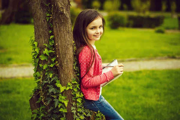 Menina com caderno e caneta perto da árvore — Fotografia de Stock