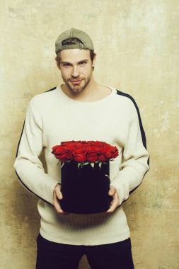 Sakallı gülümseyen adam kırmızı gül kutusu dokulu duvar tutar