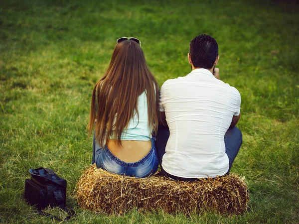 girl and man sitting on hay bale on green grass