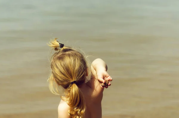 Lindo bebé niño o niña lanzando piedras en el mar azul —  Fotos de Stock