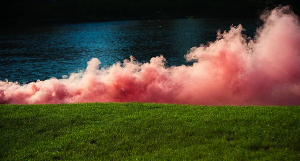 Pink smoke on green grass at river water, sport