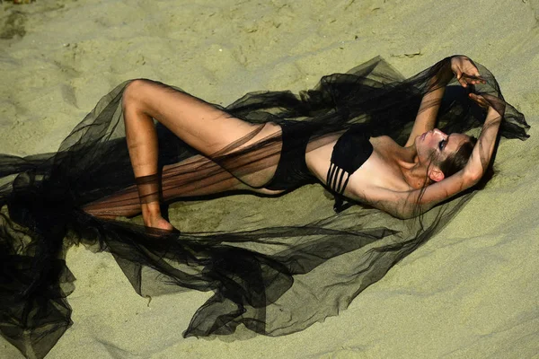 Mujer de moda en traje de baño bajo velo negro relajarse en la arena — Foto de Stock