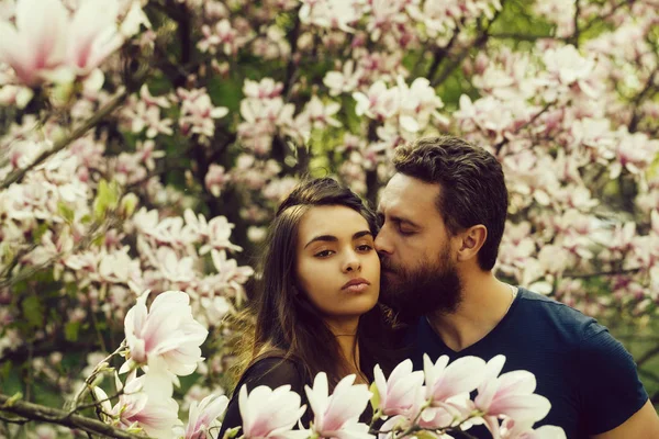 Мужчина целует милую девушку на цветущих деревьях магнолии — стоковое фото